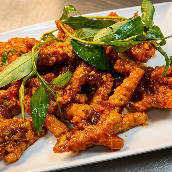 Plate of crispy chicken feet coated in spicy orange sauce, garnished with fresh green herbs.