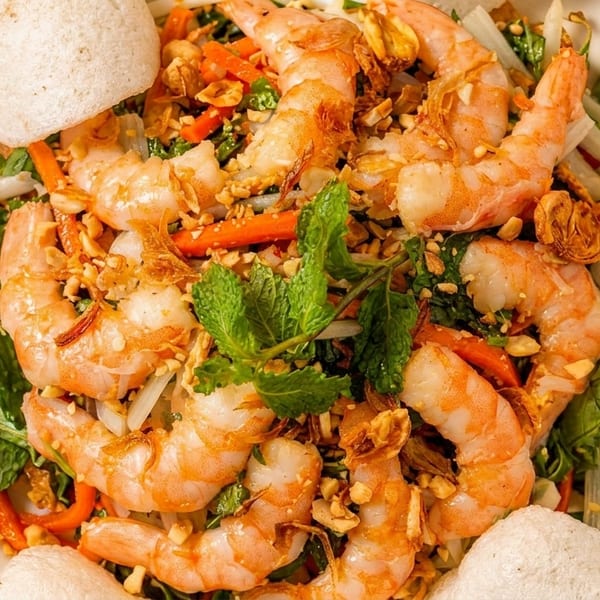 Shrimp salad with fresh mint, carrots, peanuts, and crispy rice crackers on a white plate.