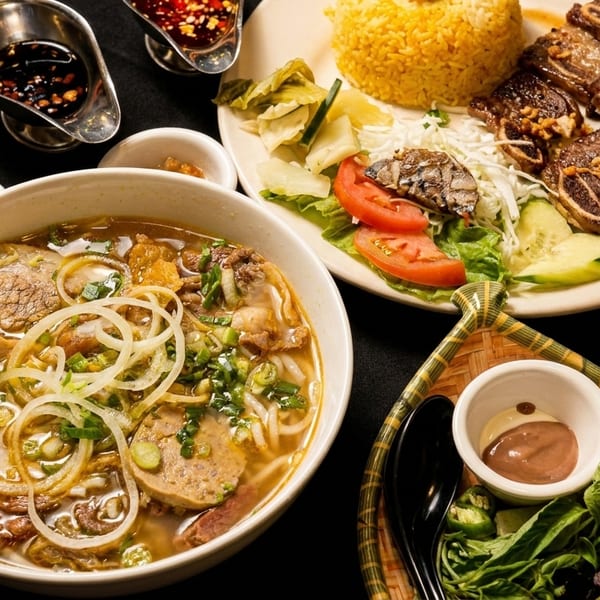 Vietnamese pho and grilled short ribs with rice, salad, and sauces on a dark table.